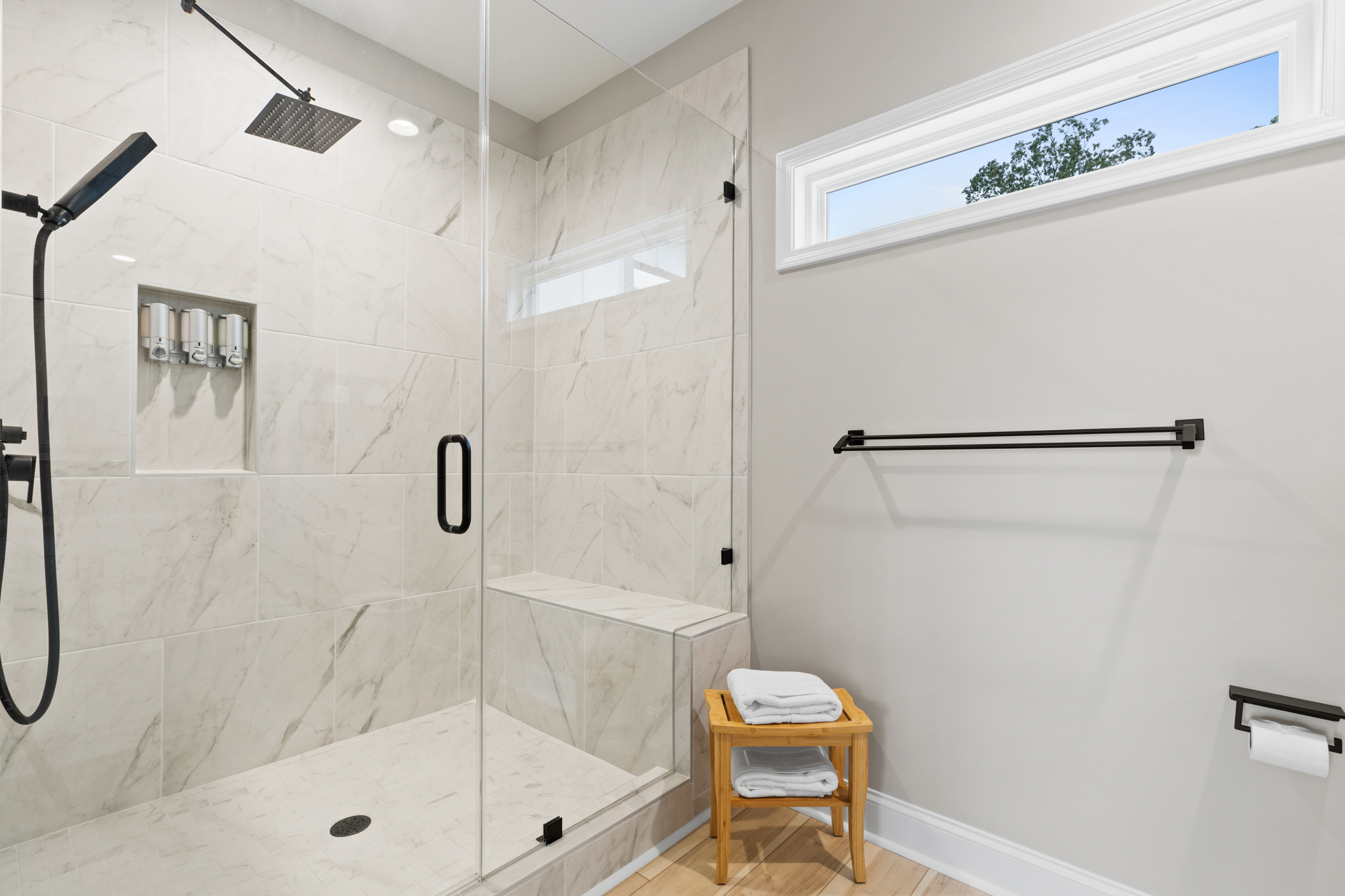 Walk-in shower with marble tile, rain head, and bench