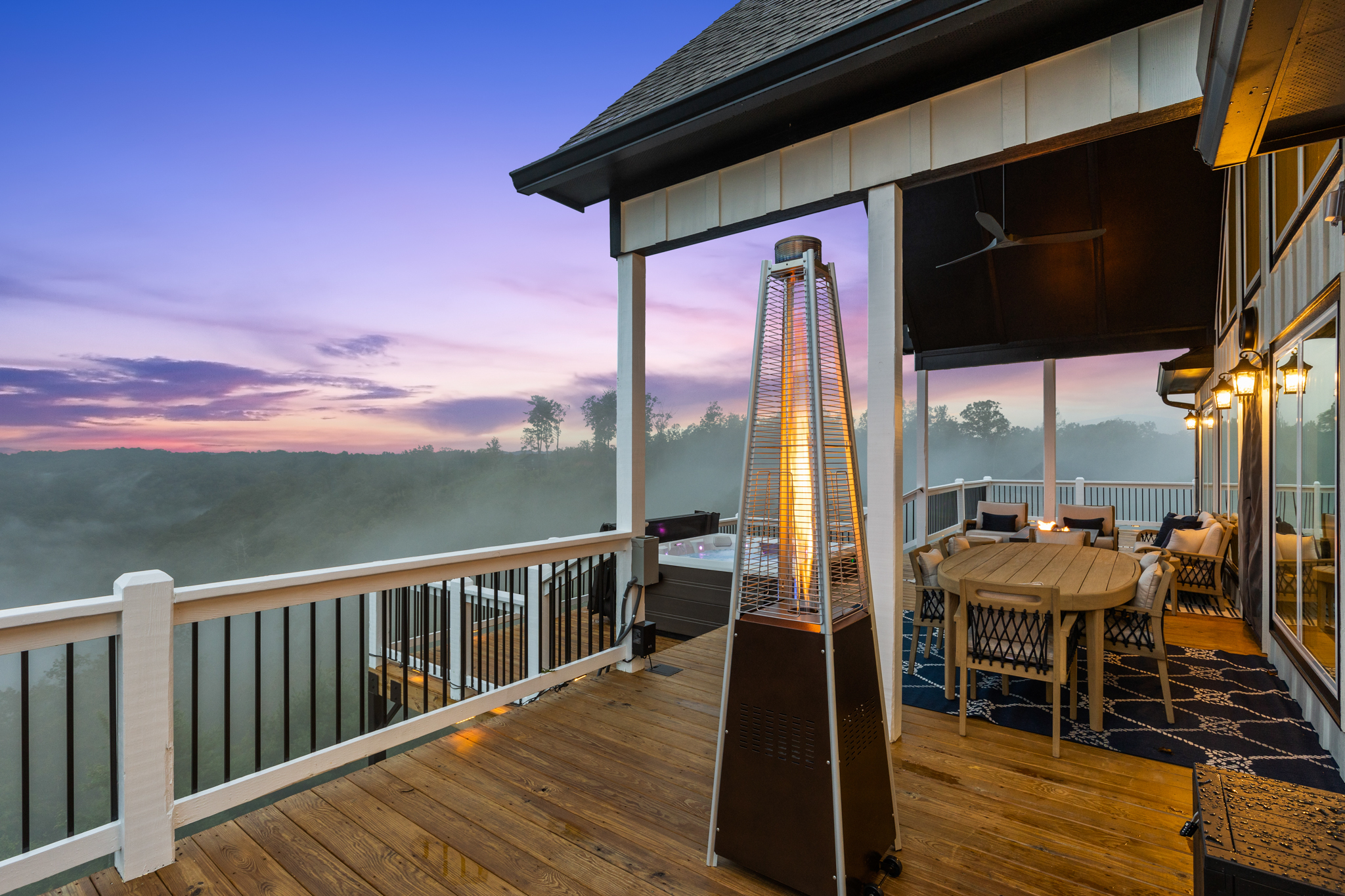 Deck with patio heater, hot tub, and sunset mist